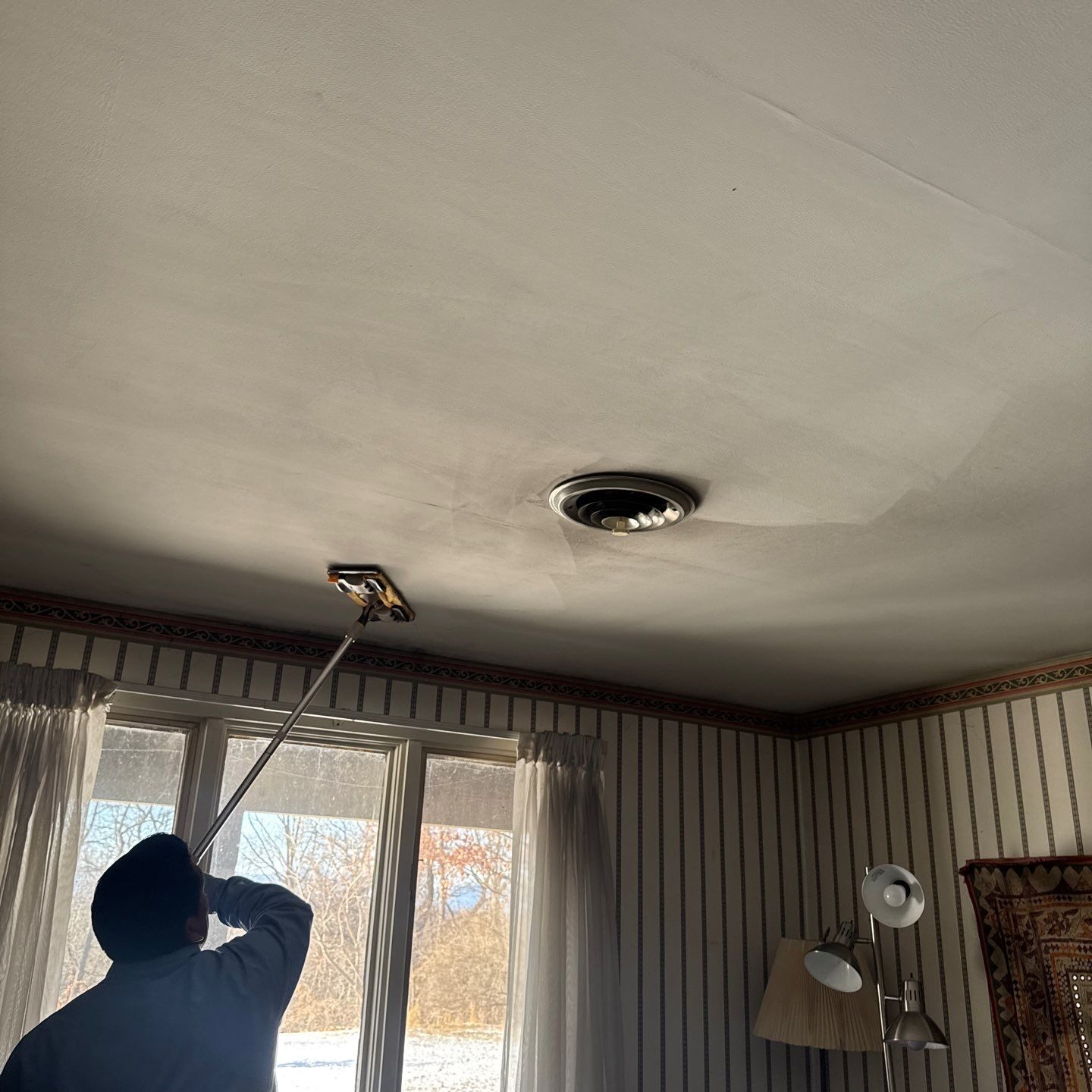 Person repairing or inspecting a ceiling vent with a long tool.
